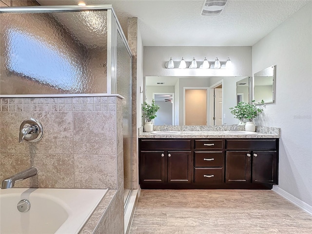 full bathroom with a tile shower, a textured ceiling, a tub, and a sink