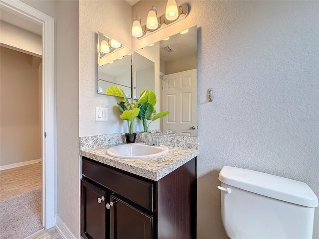 bathroom with toilet, wood finished floors, baseboards, vanity, and a textured wall