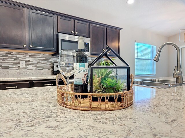 room details featuring stainless steel microwave, dark brown cabinets, backsplash, light stone countertops, and a sink