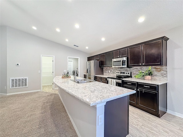 kitchen featuring visible vents, a kitchen island with sink, a sink, stainless steel appliances, and vaulted ceiling