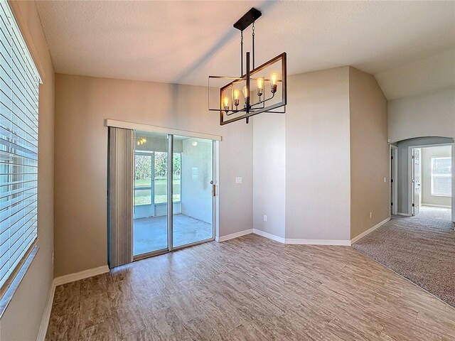 empty room featuring baseboards, wood finished floors, arched walkways, a notable chandelier, and a textured ceiling