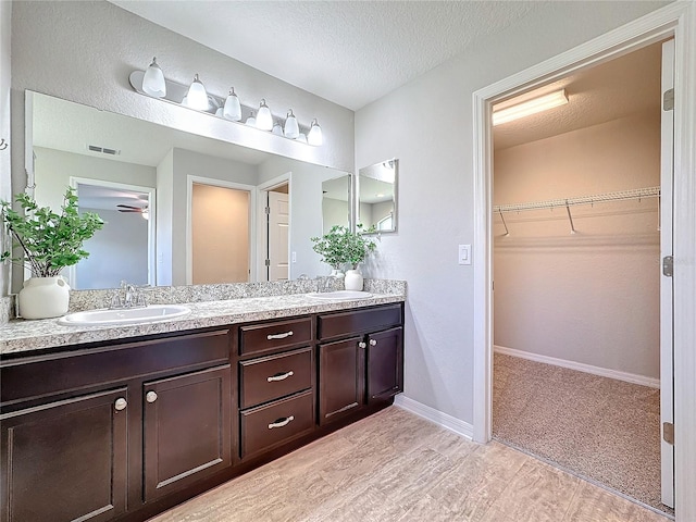 bathroom featuring a sink, visible vents, a textured ceiling, and double vanity