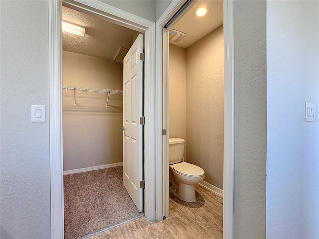 bathroom with wood finished floors, baseboards, a spacious closet, toilet, and a textured wall