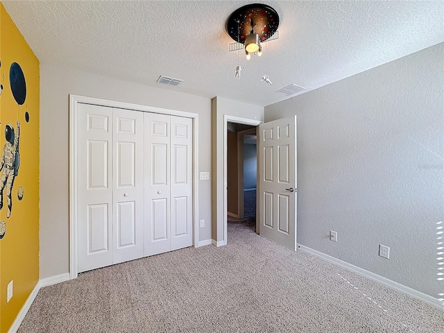 unfurnished bedroom with visible vents, a textured ceiling, a closet, carpet, and baseboards