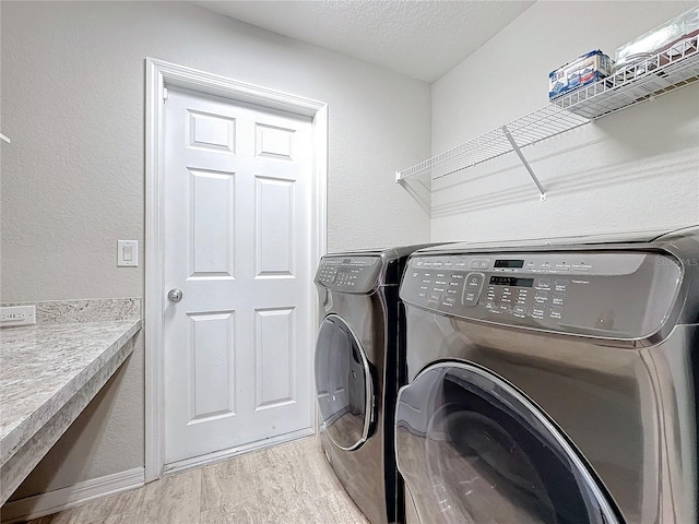 clothes washing area featuring light wood finished floors, laundry area, a textured ceiling, washer and dryer, and a textured wall