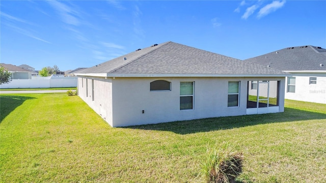 rear view of property featuring a yard, fence, roof with shingles, and stucco siding