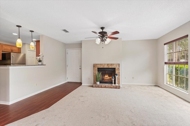 unfurnished living room with a fireplace, dark colored carpet, visible vents, a textured ceiling, and baseboards