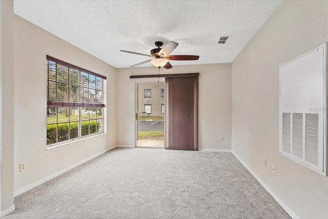 empty room featuring visible vents, light colored carpet, a ceiling fan, a textured ceiling, and baseboards