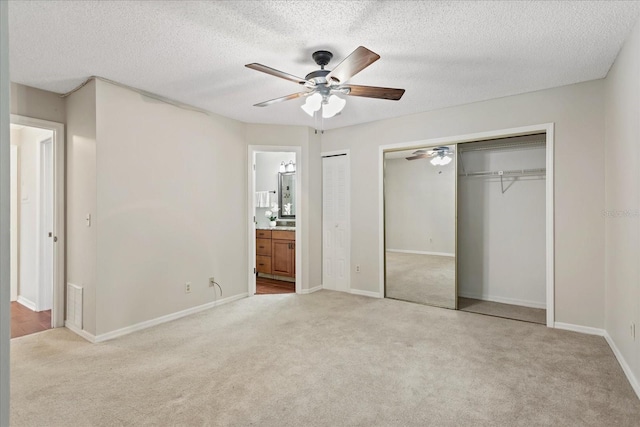 unfurnished bedroom featuring two closets, visible vents, light carpet, a textured ceiling, and ensuite bath