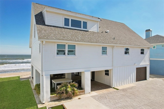 back of property featuring a water view, a garage, and a beach view