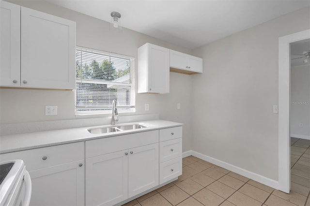 kitchen featuring stove, sink, light tile patterned floors, and white cabinets