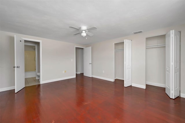 unfurnished bedroom with ceiling fan, dark wood-type flooring, and multiple closets