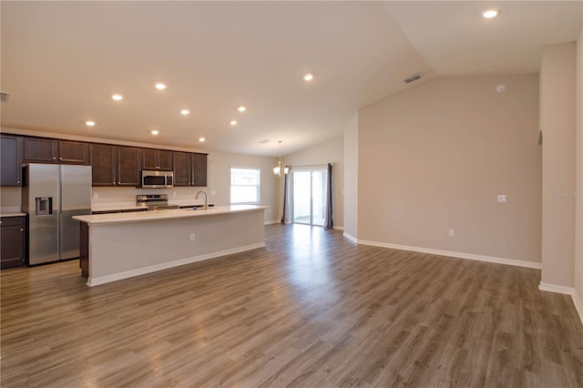 kitchen featuring vaulted ceiling, appliances with stainless steel finishes, an island with sink, wood-type flooring, and dark brown cabinetry