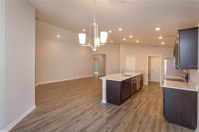 kitchen featuring sink, dark brown cabinets, light wood-type flooring, pendant lighting, and a kitchen island with sink