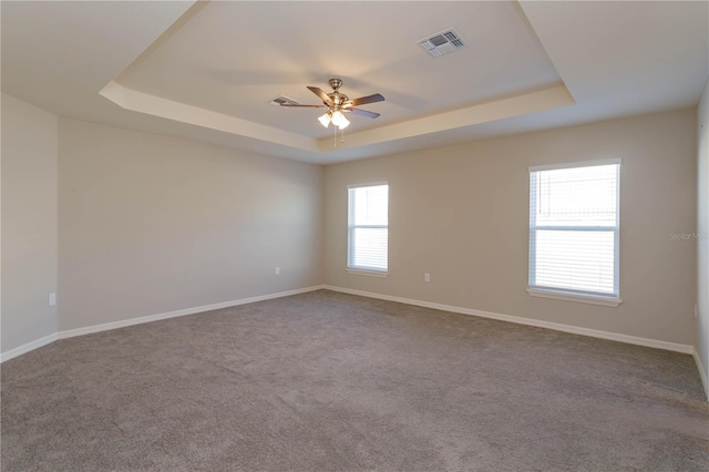 carpeted spare room with a raised ceiling and ceiling fan