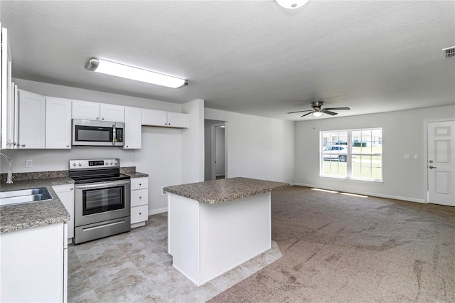 kitchen featuring sink, appliances with stainless steel finishes, white cabinetry, a textured ceiling, and a kitchen island