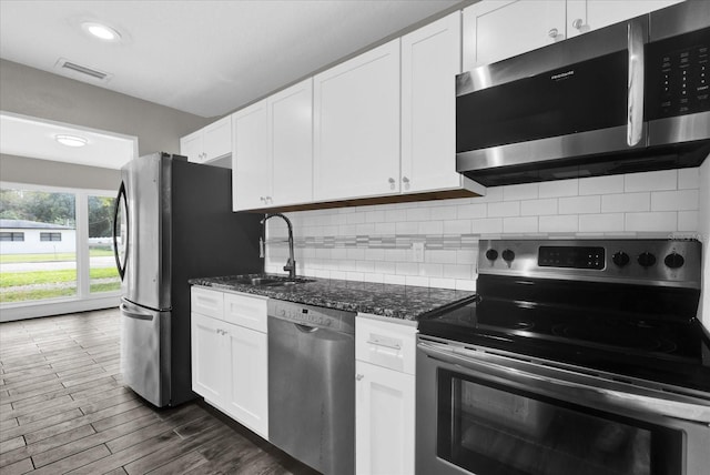 kitchen featuring sink, white cabinetry, dark stone countertops, stainless steel appliances, and backsplash