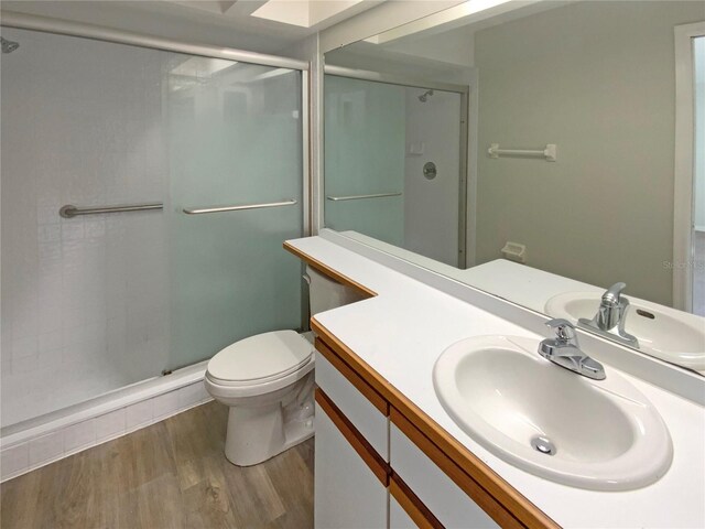 bathroom featuring toilet, hardwood / wood-style flooring, a shower with shower door, and vanity