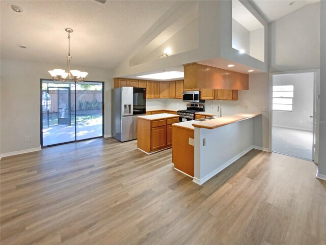 kitchen featuring light wood-type flooring, kitchen peninsula, hanging light fixtures, stainless steel appliances, and a chandelier