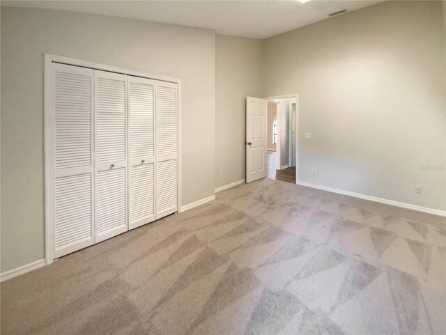 unfurnished bedroom featuring a high ceiling, a closet, and light colored carpet