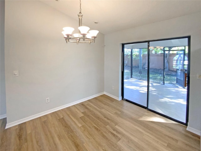 spare room featuring a notable chandelier, light wood-type flooring, and vaulted ceiling