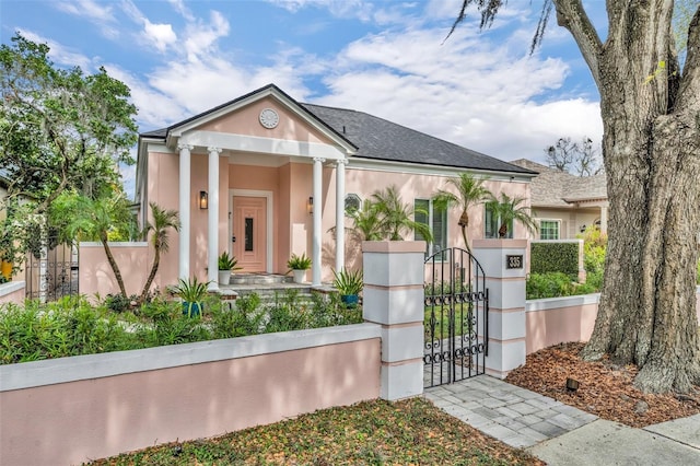 neoclassical / greek revival house featuring stucco siding, a fenced front yard, and a gate