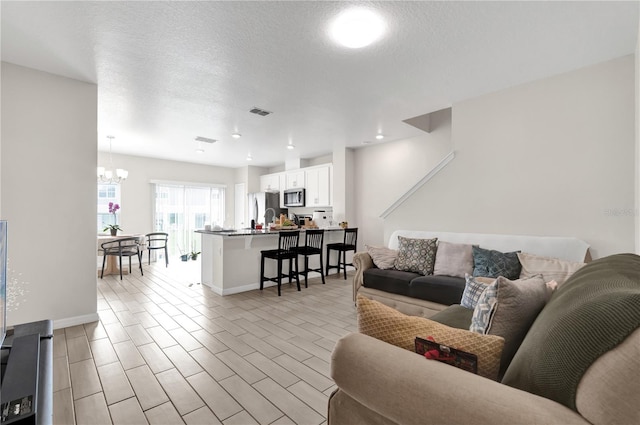 living room with light hardwood / wood-style floors, a textured ceiling, and a notable chandelier