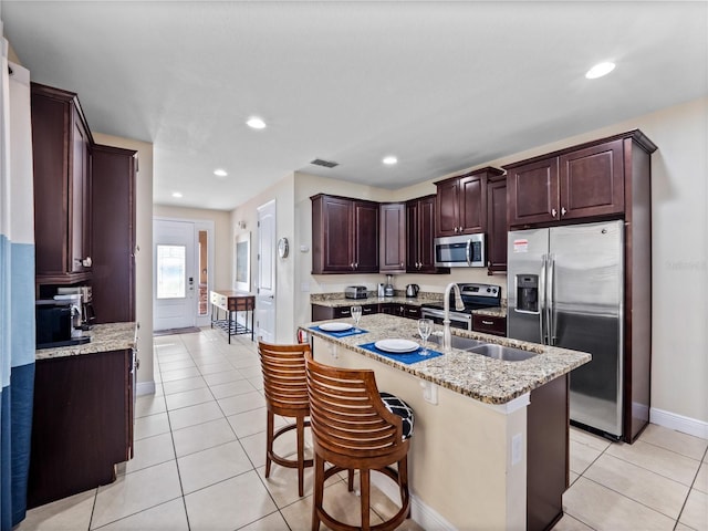 kitchen with sink, appliances with stainless steel finishes, a kitchen breakfast bar, light stone countertops, and an island with sink