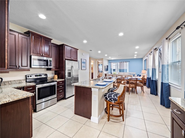 kitchen featuring light stone countertops, an island with sink, appliances with stainless steel finishes, and light tile patterned floors