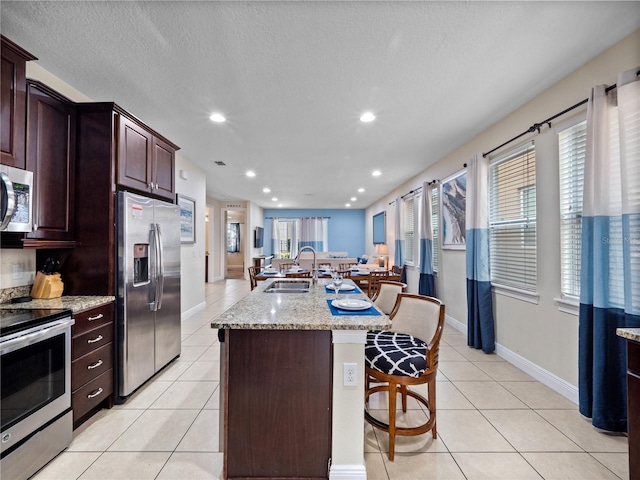 kitchen featuring sink, light tile patterned floors, stainless steel appliances, and a center island with sink