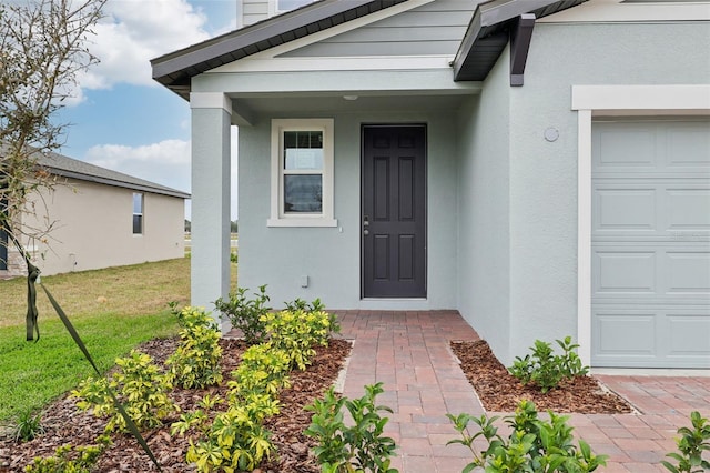 entrance to property with a garage, a lawn, and stucco siding