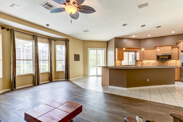 kitchen featuring pendant lighting, light hardwood / wood-style flooring, appliances with stainless steel finishes, backsplash, and light brown cabinetry