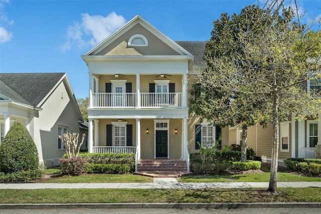 greek revival inspired property featuring brick siding, a balcony, ceiling fan, a porch, and stucco siding