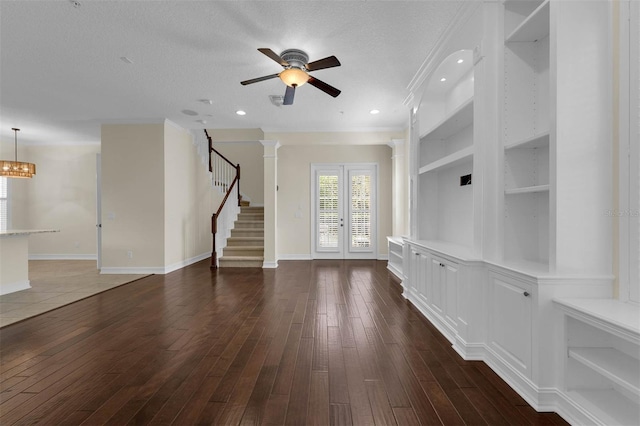 unfurnished living room featuring built in features, dark wood-style flooring, a textured ceiling, and stairs