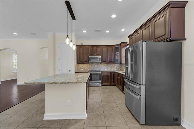 kitchen featuring arched walkways, light tile patterned floors, decorative backsplash, appliances with stainless steel finishes, and a kitchen island