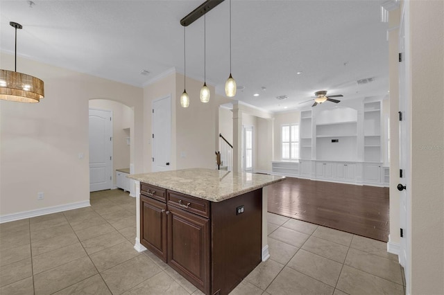 kitchen featuring light tile patterned floors, arched walkways, built in shelves, hanging light fixtures, and crown molding