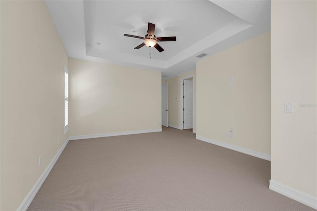 carpeted spare room featuring baseboards, visible vents, a tray ceiling, and ceiling fan