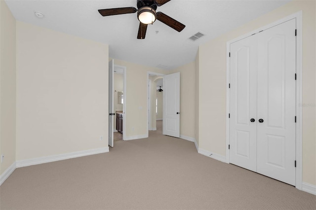 unfurnished bedroom with baseboards, visible vents, a ceiling fan, light colored carpet, and a closet