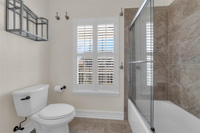 bathroom featuring toilet, plenty of natural light, enclosed tub / shower combo, and baseboards