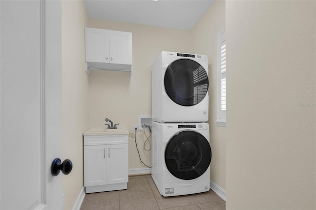 washroom with stacked washer and clothes dryer, cabinet space, light tile patterned flooring, a sink, and baseboards