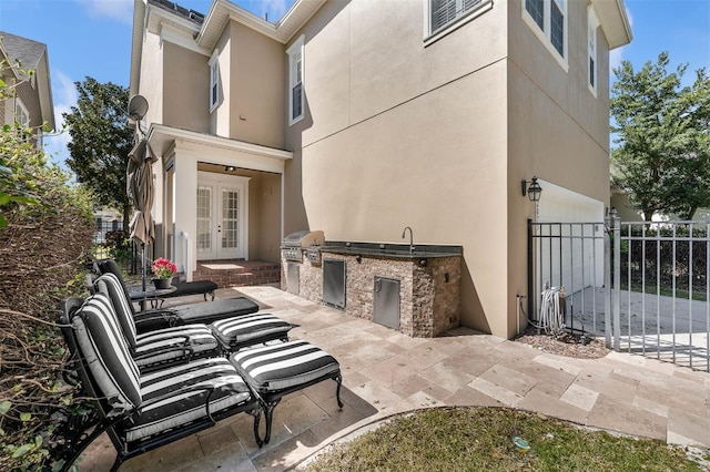 view of patio featuring french doors, an outdoor kitchen, a grill, fence, and a sink