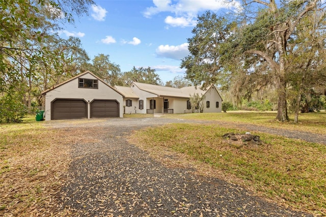 ranch-style home featuring a garage, gravel driveway, and stucco siding