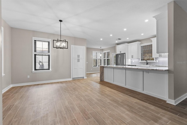 kitchen featuring light stone counters, backsplash, light wood-style flooring, freestanding refrigerator, and white cabinets