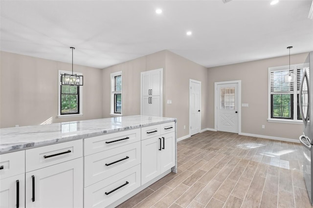 kitchen featuring light stone counters, white cabinets, decorative light fixtures, and baseboards
