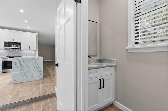 interior space featuring appliances with stainless steel finishes, wood tiled floor, white cabinets, and tasteful backsplash