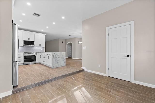 kitchen featuring arched walkways, stainless steel appliances, visible vents, wood tiled floor, and white cabinetry
