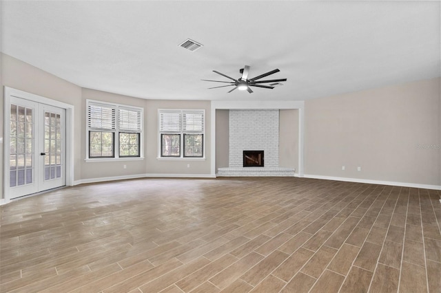 unfurnished living room with visible vents, a ceiling fan, french doors, light wood-type flooring, and a fireplace