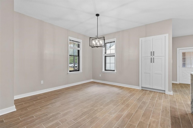 unfurnished room with a notable chandelier, light wood-style flooring, and baseboards