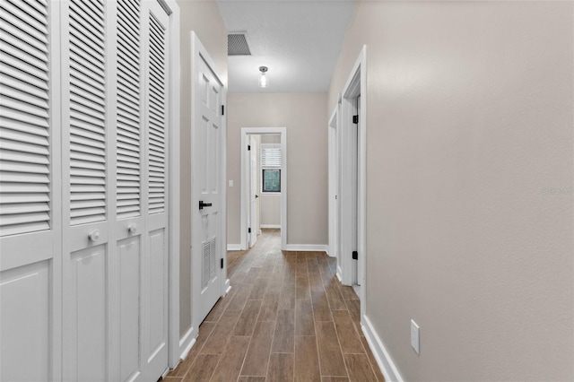 hall featuring wood tiled floor, visible vents, and baseboards