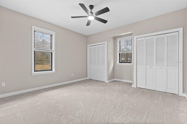 unfurnished bedroom with a ceiling fan, carpet, baseboards, and two closets